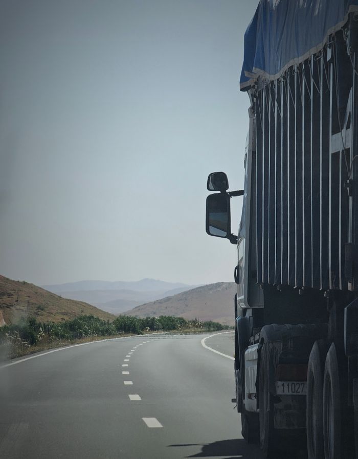 pexels-photo-16180770-16180770 Truck on a winding highway in Douar Ouled El Mesnaoui, Morocco, set in a rocky landscape.